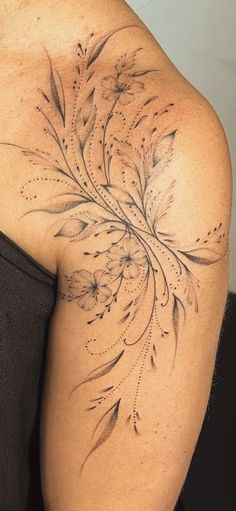 the back of a woman's shoulder with flowers and leaves tattoo on her left arm