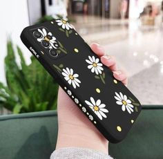 a woman holding up her phone case with daisies on it