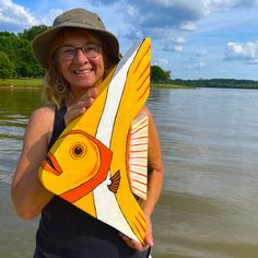 a woman holding up a yellow fish shaped surfboard