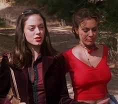 two young women walking down a dirt road in the woods, one wearing a red top