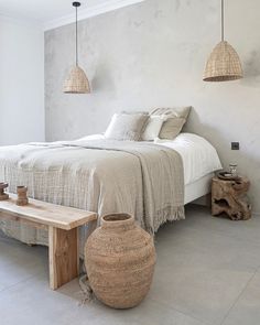 a bedroom with white walls and flooring, two hanging lights above the headboard