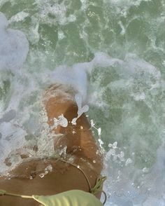 a woman laying on top of a sandy beach next to the ocean with waves coming in