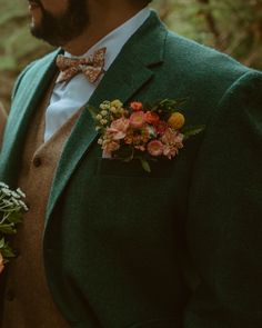 a man wearing a green suit and bow tie holding flowers in his hand while standing next to another man