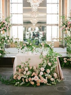 a table with flowers and greenery on it in front of a chandelier