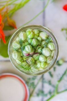 a jar filled with green vegetables next to some flowers