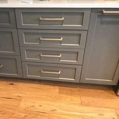 a kitchen with gray cabinets and white counter tops, wood flooring in front of the sink