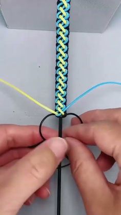 two hands are working on a piece of blue and yellow string with one hand holding the end