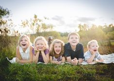 four children laying on a blanket in the grass with their mouths open and smiling at the camera