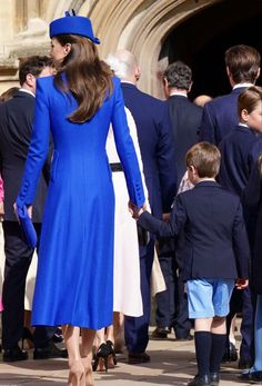 a woman in a blue and white dress holding hands with a little boy wearing a suit