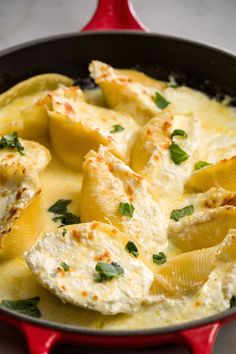 a red skillet filled with pasta and chicken covered in cheese, sauce and parsley