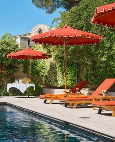 an outdoor pool with lounge chairs and umbrellas next to the swimming pool, surrounded by greenery