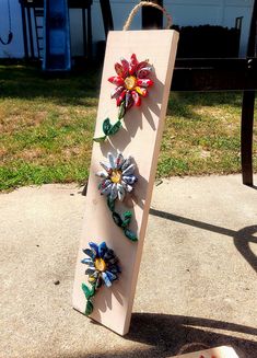 three colorful flowers are attached to a wooden board on the ground near a bench and grass