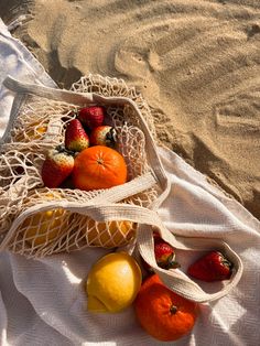 strawberries, oranges and lemons in a mesh bag on the sand at the beach