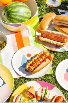 a table topped with plates filled with sandwiches and hot dogs next to watermelon