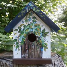 a birdhouse painted with leaves and flowers on it's roof is sitting on a tree stump