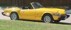 an old yellow sports car parked on the side of the road in front of a house