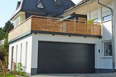 a white house with a wooden balcony on the top floor and an attached garage door