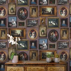 a wall with many pictures on it and flowers in vases next to an old dresser