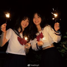 two young women holding sparklers in their hands at night, both wearing school uniforms