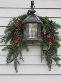 a lantern hanging from the side of a house decorated with pine cones and red berries