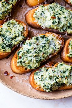 several pieces of bread with cheese and spinach spread on them sitting on a plate