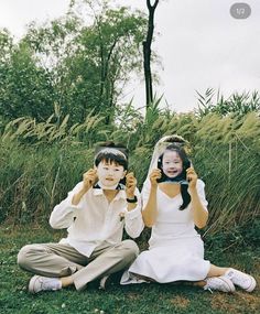 two children sitting on the ground holding up their cell phones in front of their faces