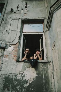 two people sitting on the window sill of an old building