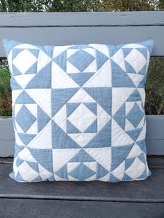 a blue and white quilted pillow sitting on top of a wooden bench next to trees