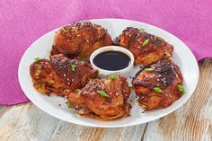 a white plate topped with chicken wings next to a cup of black sauce on top of a wooden table