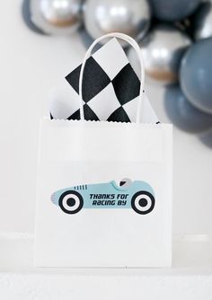 a white bag with a blue race car on it and some balloons in the background