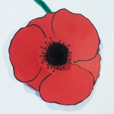 a paper poppy with a black center and green stamen on the middle, sitting on a white surface