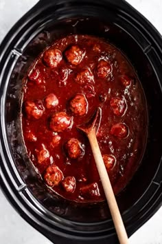 a wooden spoon in a slow cooker filled with meatballs and tomato marinara sauce