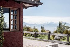 an open window on the side of a red building with mountains in the back ground