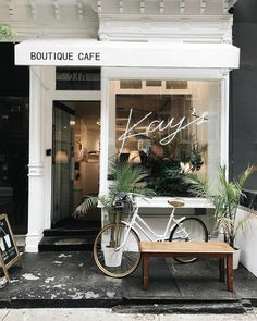 a white bicycle parked in front of a store window with potted plants on the sidewalk