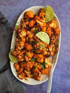 a white plate topped with cauliflower next to a fork and lime wedges