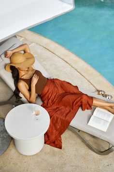 a woman laying on top of a white chair next to a pool with a book