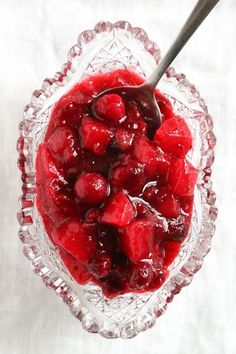 a glass bowl filled with cherries on top of a white cloth covered tablecloth