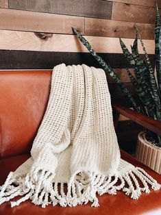 a white knitted blanket sitting on top of a brown leather chair next to a potted plant