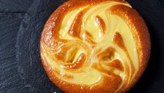 a pastry with yellow icing on it sitting on a black surface next to a spoon