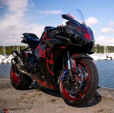 a red and black motorcycle parked next to the water