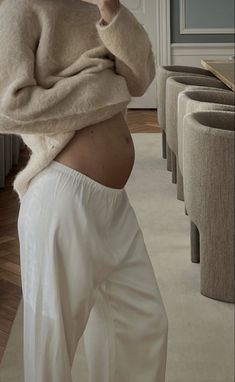 the pregnant woman is wearing white pants and a sweater