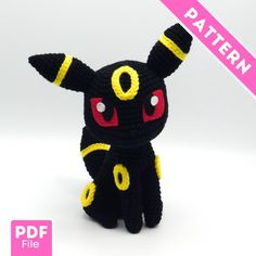 a black and yellow knitted toy with red eyes sitting on a white table top