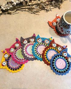 several crocheted owl coasters on a table next to a coffee cup