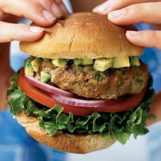 two hands holding a hamburger with lettuce and tomatoes