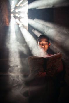 a boy reading a book in the dark with beams of light coming from behind him