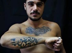 a man with arabic writing on his arm and chest is posing for the camera in front of a black background