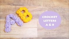 two crochet letters are sitting on a wooden surface and one is yellow, the other is purple