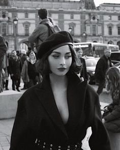 a woman walking down the street in a black dress and beret with her hands on her hips