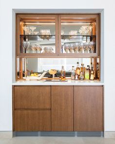 a kitchen with wooden cabinets and white counter tops, filled with glasses on the top shelf