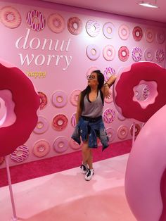 a woman standing in front of donuts on display at a doughnut shop with pink walls